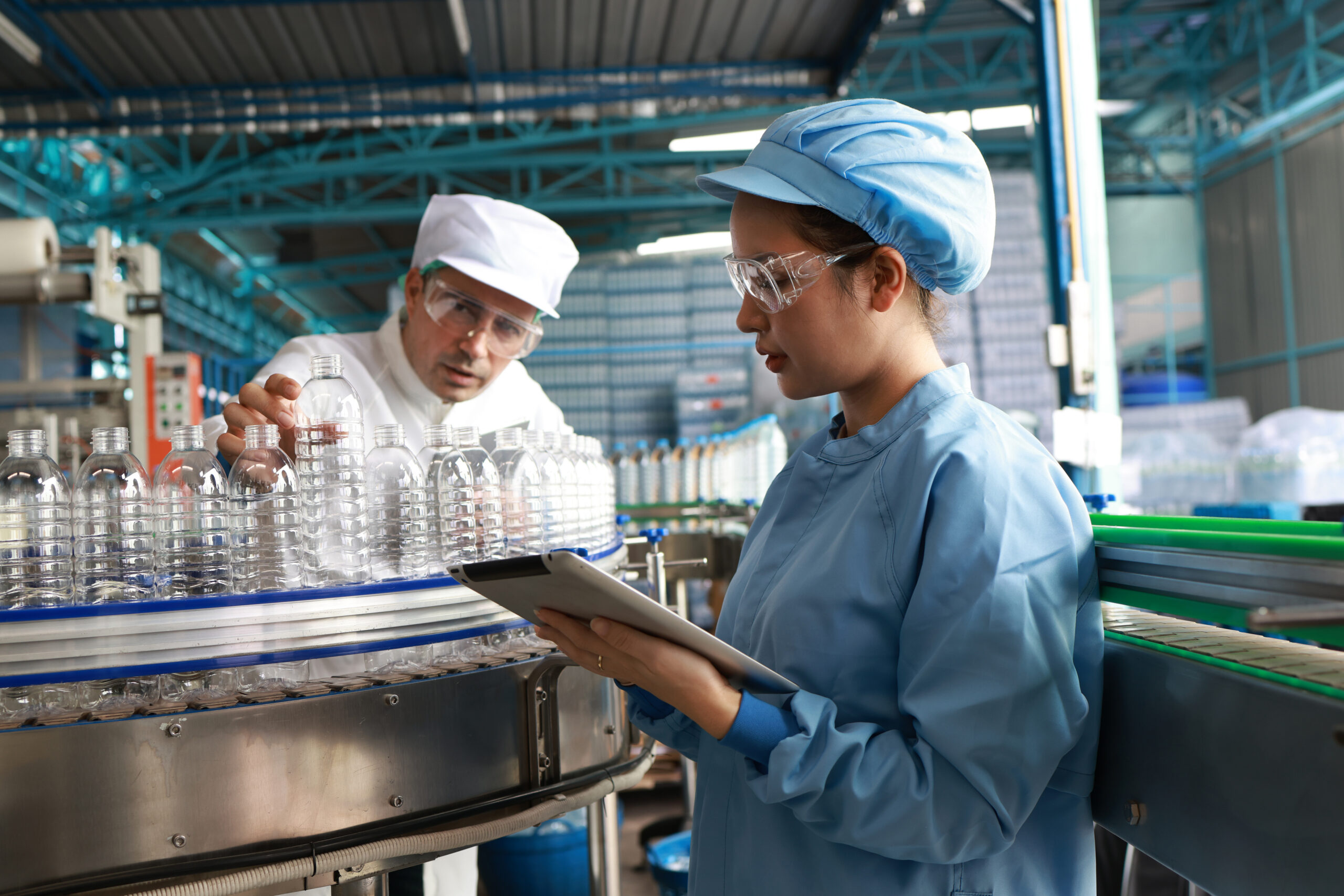 The lab technicians and hygienists with clean suits and PPE examining water bottles in bottling plant mineral water drinking water factory